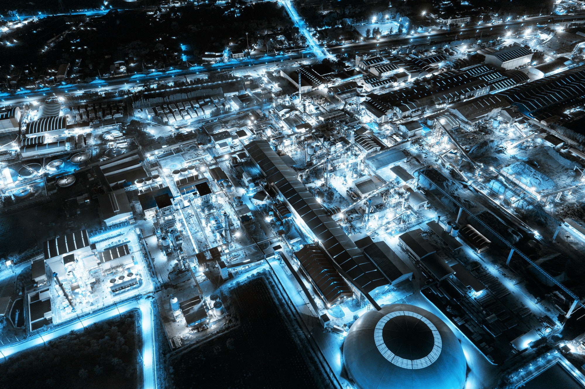 Blue light industrial factory with chemical refinery and building material glowing light at night
